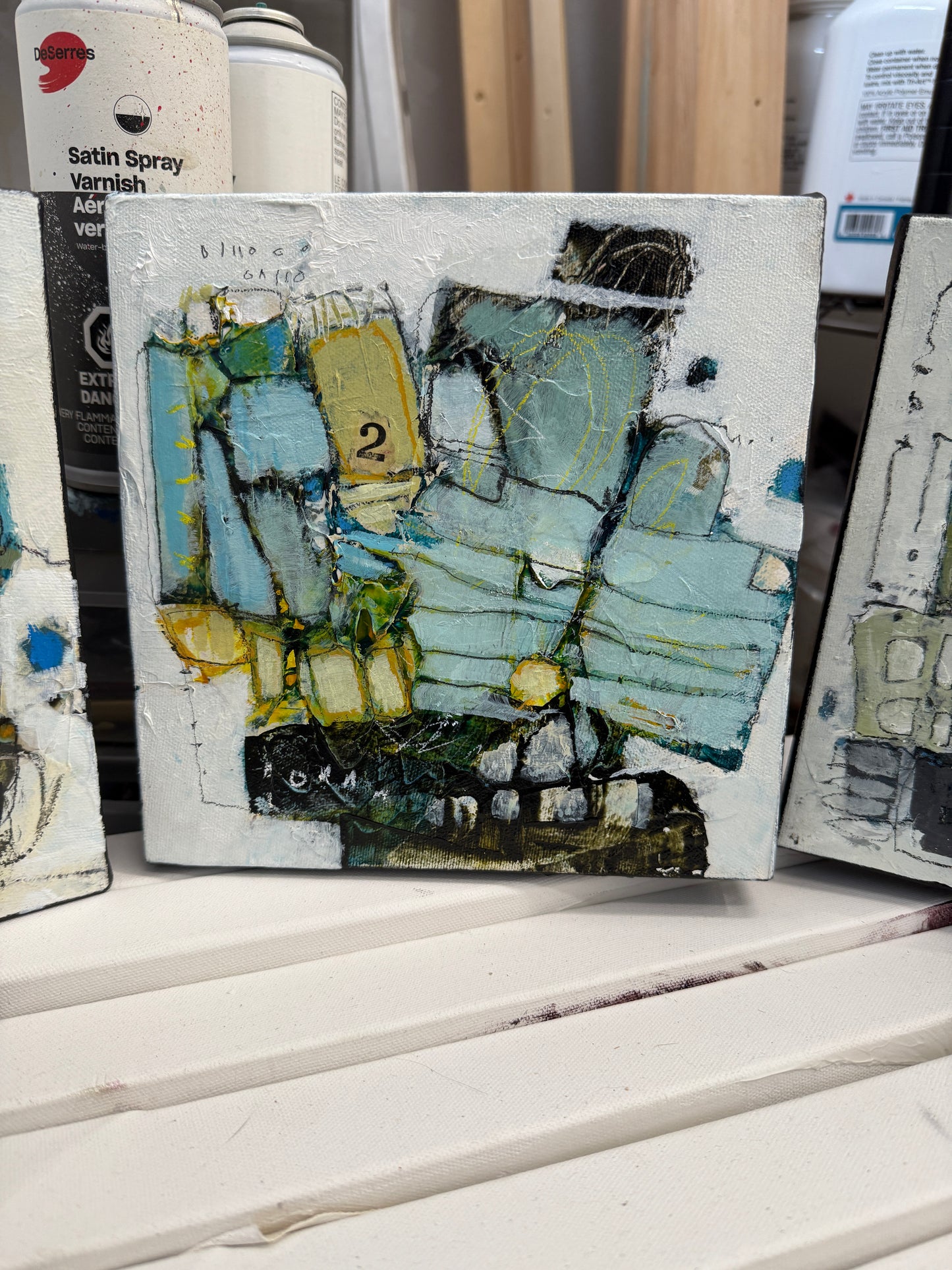 Small abstract painting on a white surface with art supplies in the background