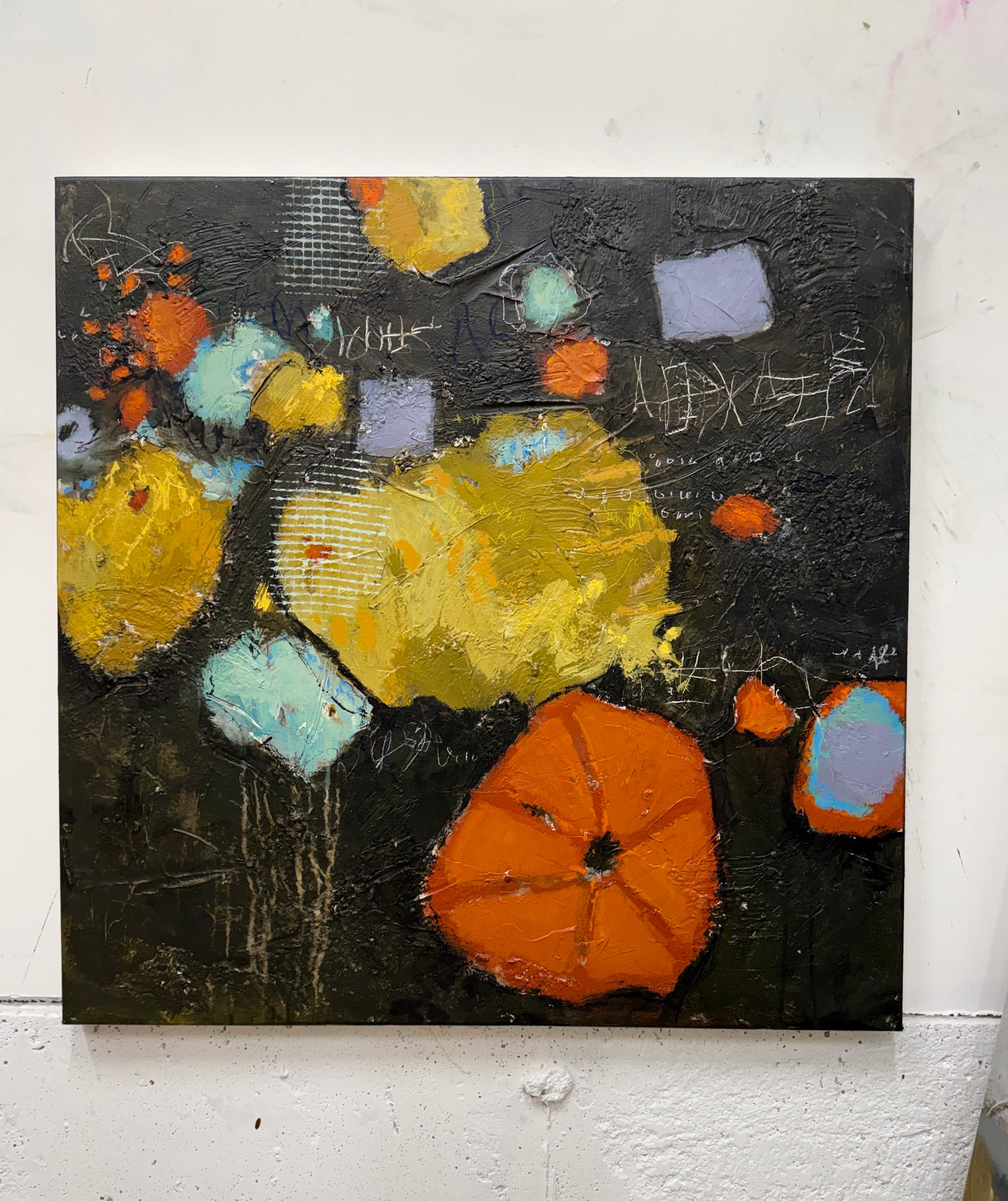 An abstract canvas painting featuring textured impasto brushstrokes in yellow, orange, light blue, and lavender on a dark charcoal-black background, displayed on a white wall.