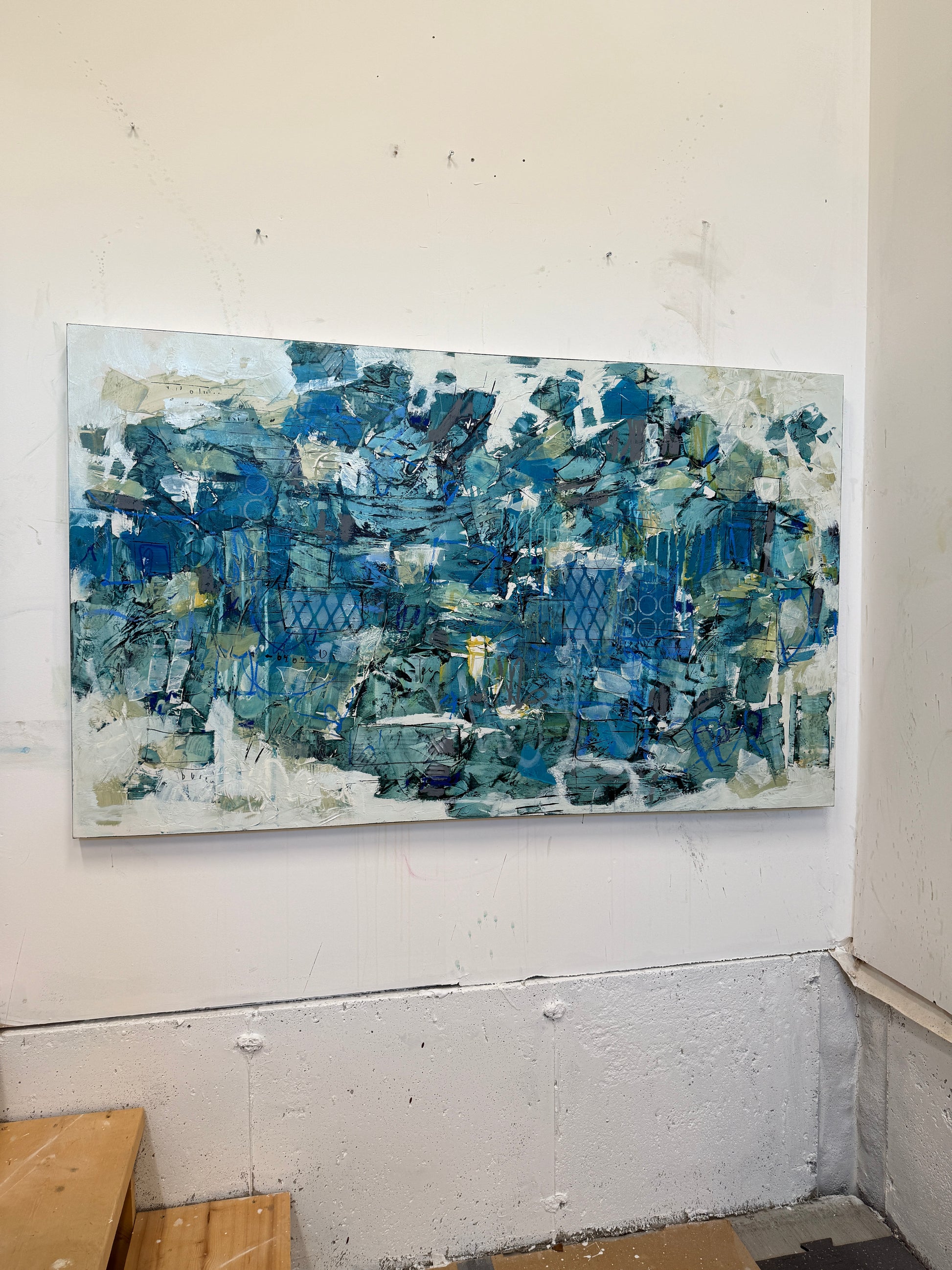Large 48 x 72 inch abstract acrylic painting on canvas by Canadian artist Lori Mirabelli, featuring layered shades of deep and muted blue with hints of green, white, and texture, displayed above a cozy white bed with soft blue bedding in a modern minimalist bedroom. Contemporary fine art by Toronto-based abstract painter Lori Mirabelli, collected in homes across Canada and the U.S.
