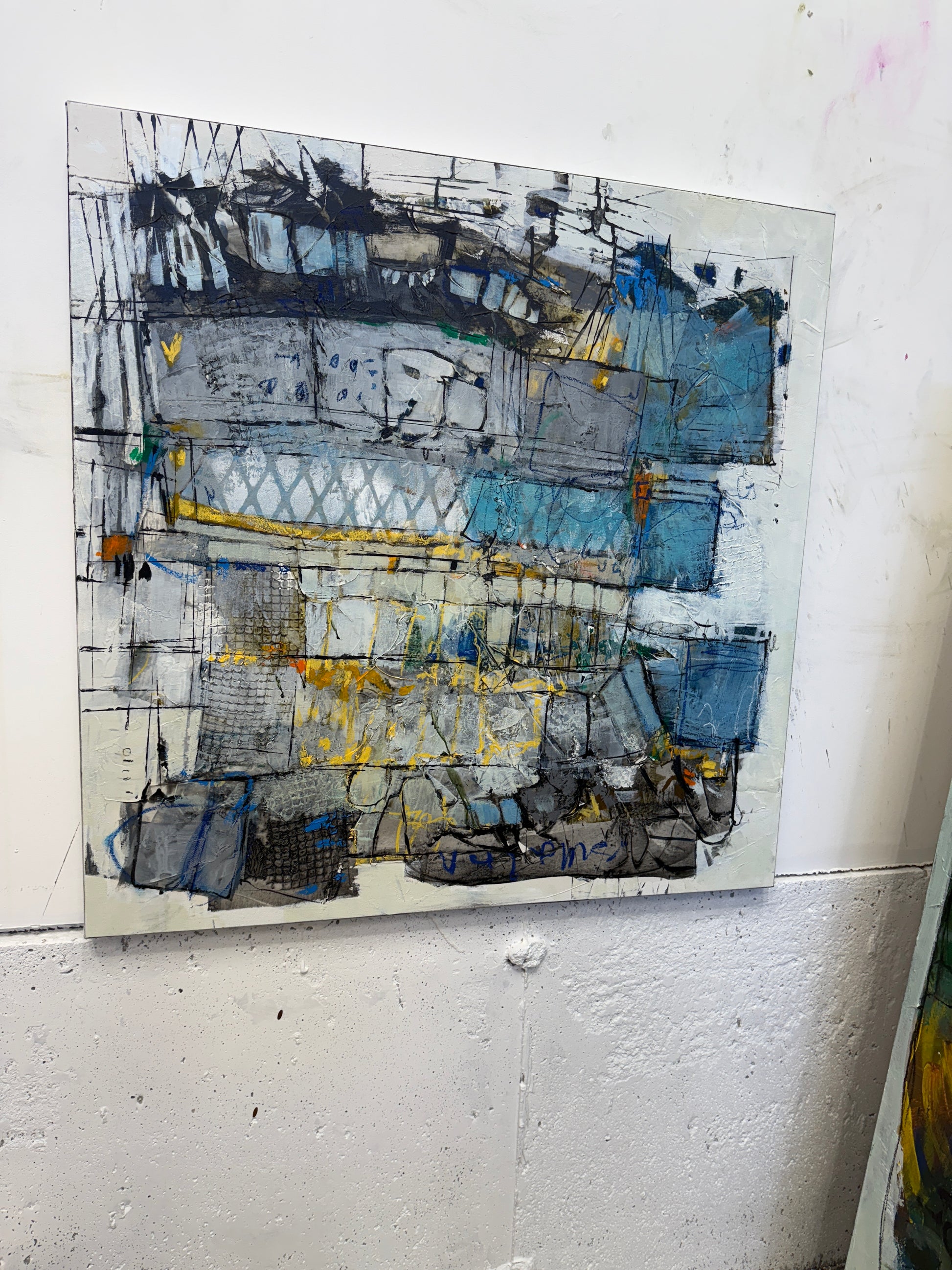 30x30 inch abstract acrylic painting on canvas featuring layered geometric shapes in grey, blue, and white with pops of bright yellow. The surface has rich texture, visible brushstrokes, and mark-making that gives it an urban, architectural feel with hints of movement and depth lori mirabelli