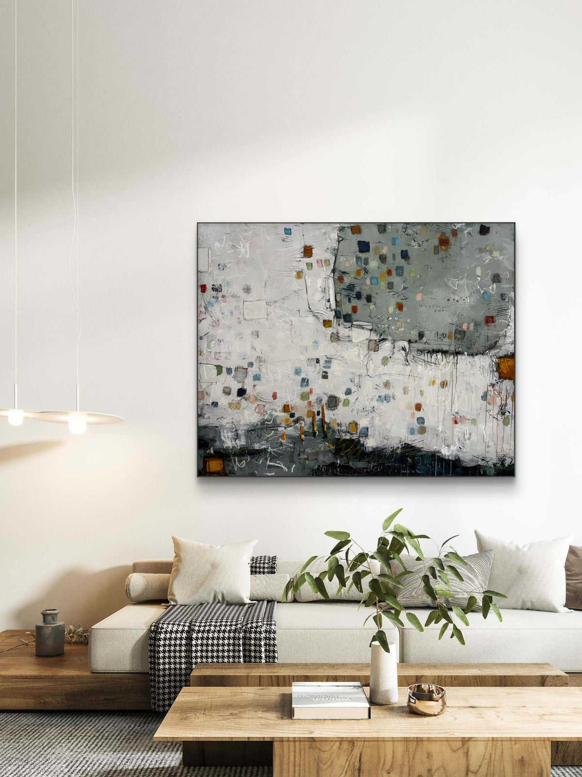 Large 48 × 60-inch abstract painting with textured white and sage-grey fields, scattered small squares in blue, mustard, rust, pink and green, and loose black and white lines. Dark charcoal layers anchor the bottom edge. The painting hangs above a black leather chair with wooden arms against a light wall.