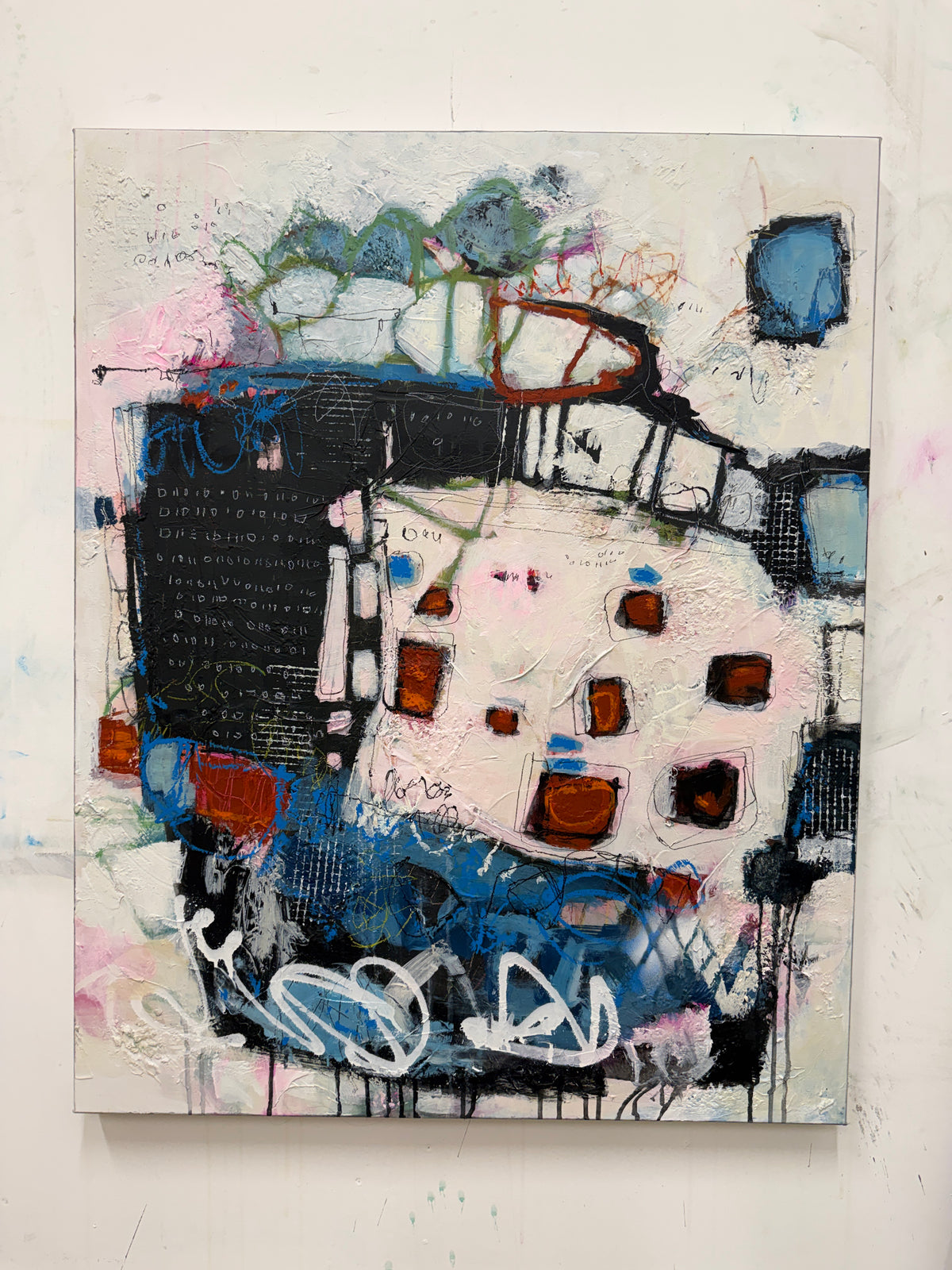 An abstract mixed-media painting on canvas featuring layered textures of black, white, blue, pink, and rust-orange paint, displayed against a white wall.