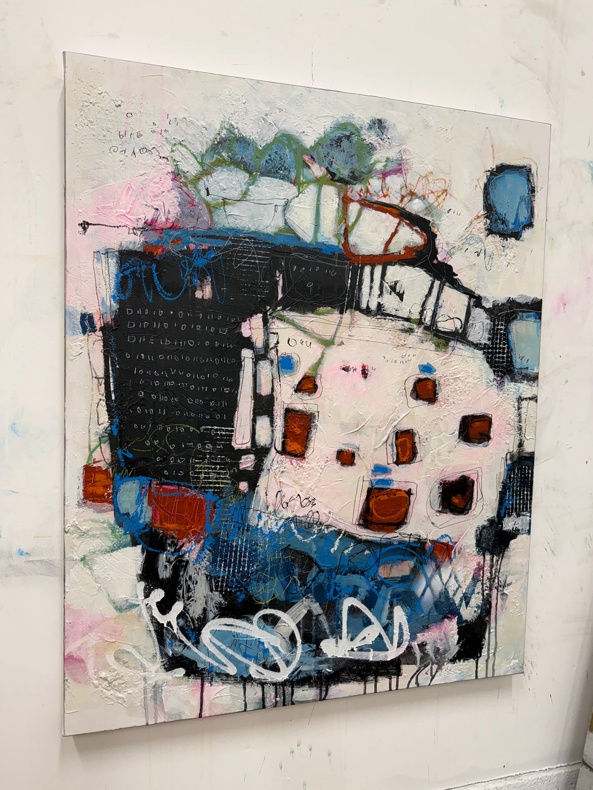 An abstract mixed-media painting on canvas, featuring textured layers of black, blue, white, pink, and brown, hanging on a white wall.