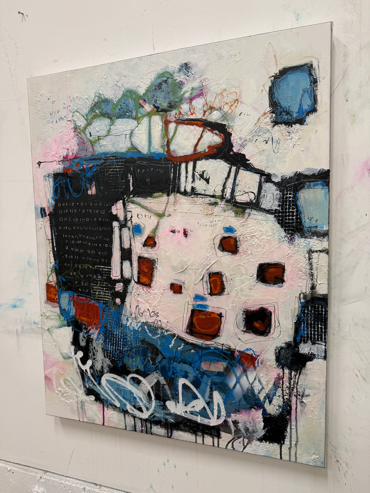 An abstract mixed-media painting on a square canvas, featuring expressive brushstrokes in blue, black, white, pink, and brown, displayed on a white wall.